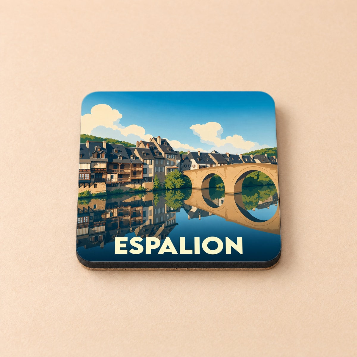 Dessous de verre souvenir de la ville d'Espalion avec une illustration stylisée du vieux pont et des maisons à colombages se reflétant dans le Lot.
