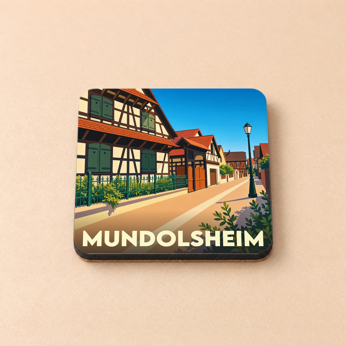Dessous de verre souvenir de la ville de Mundolsheim avec une illustration stylisée de maisons à colombages alsaciennes.