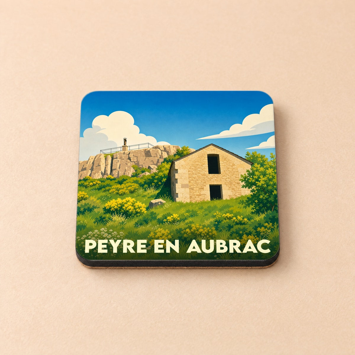 Dessous de verre souvenir de la ville de Peyre en Aubrac avec une illustration stylisée d'une bâtisse en pierre.