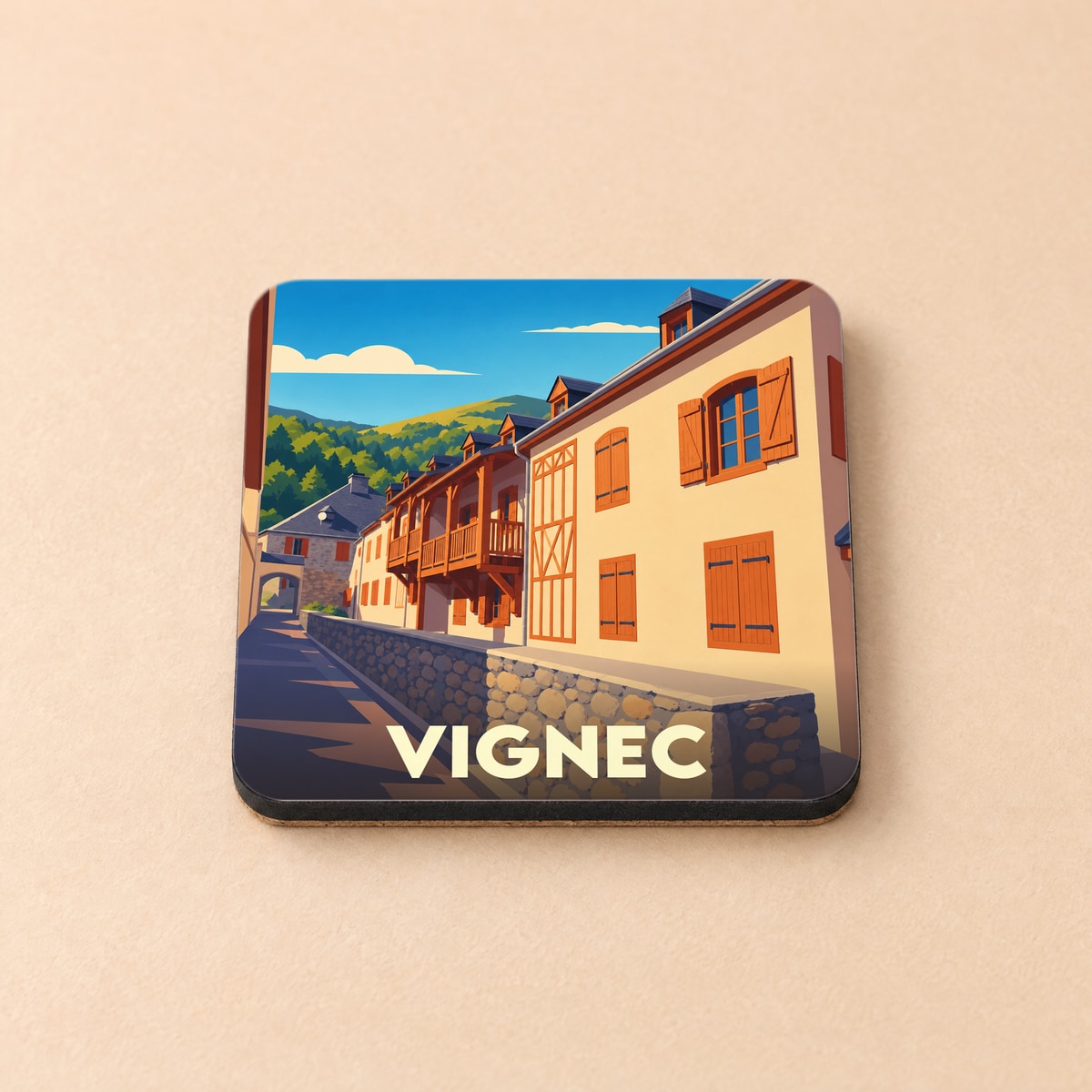 Dessous de verre souvenir de la ville de Vignec avec une illustration stylisée de maisons typiques pyrénéennes.