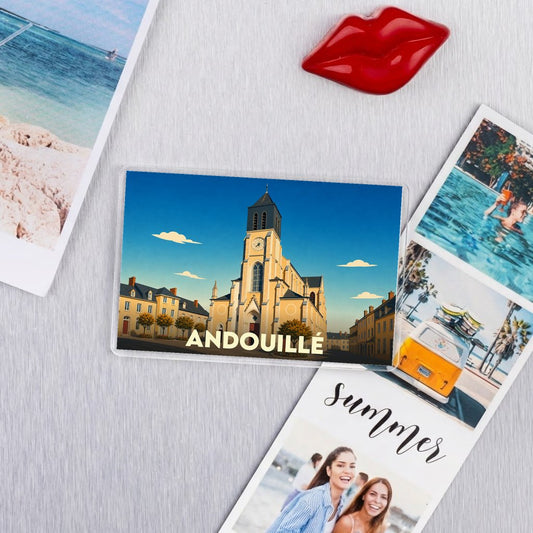 Magnat souvenir de la ville d'Andouillé avec une illustration stylisée de son église sous un ciel bleu.