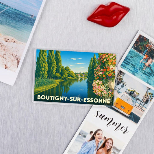 Magnet souvenir de la ville de Boutigny-sur-Essonne avec une illustration stylisée d'un paysage de rivière bordée d'arbres et de fleurs.