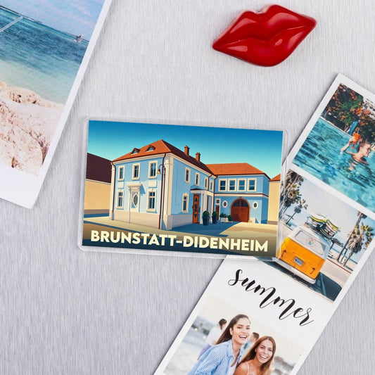 Magnet souvenir de la ville de Brunstatt-Didenheim avec une illustration stylisée d'un bâtiment bleu.