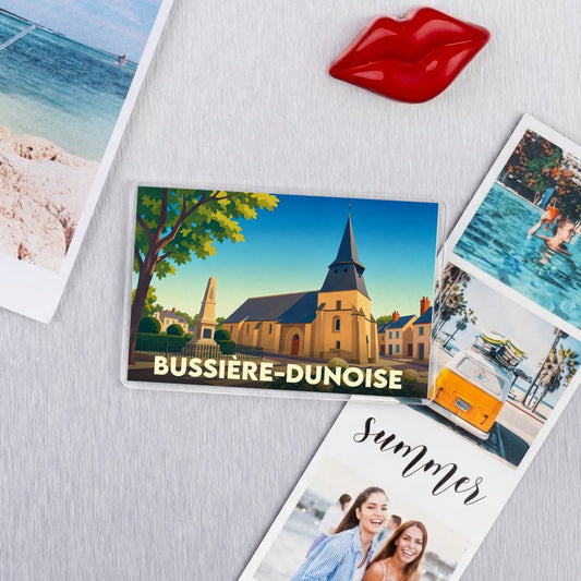 Magnet souvenir de la ville de Bussière-Dunoise avec une illustration stylisée de son église et de son monument aux morts.