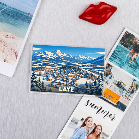 Magnet souvenir de la ville de Laye avec une illustration stylisée d'un village de montagne enneigé.