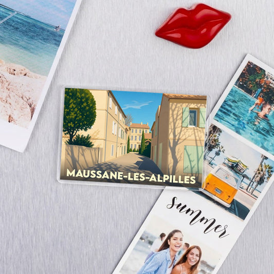 Magnet souvenir de la ville de Maussane-les-Alpilles avec une illustration stylisée d'une ruelle provençale.