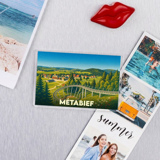 Magnet souvenir de la ville de Métabief avec une illustration stylisée d'un paysage de montagne et d'une luge d'été.