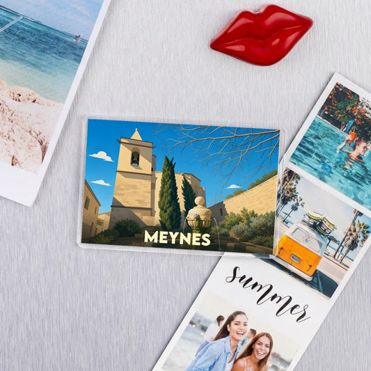 Magnet souvenir de la ville de Meynes avec une illustration stylisée de son église et de sa fontaine.