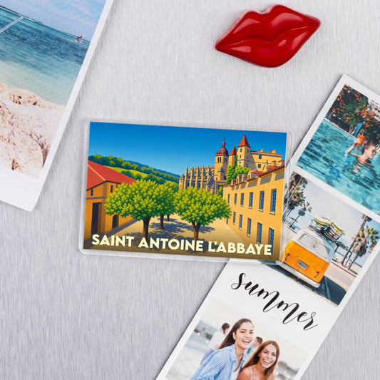 Magnet souvenir de la ville de Saint-Antoine-l'Abbaye avec une illustration colorée et stylisée de son patrimoine architectural.