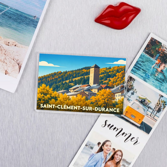 Magnet souvenir de Saint-Clément-sur-Durance représentant une illustration stylisée du village et de sa tour sous un ciel bleu.