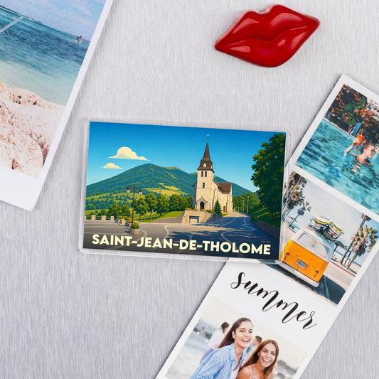 Magnet souvenir de la ville de Saint-Jean-de-Tholome avec une illustration stylisée de son église et des montagnes environnantes.