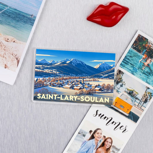 Magnet souvenir de la ville de Saint-Lary-Soulan avec une illustration montrant un village enneigé au pied des montagnes.
