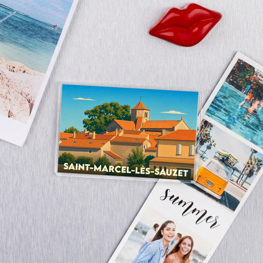 Magnet souvenir de la ville de Saint-Marcel-lès-Sauzet avec une illustration stylisée de ses toits et de son clocher.