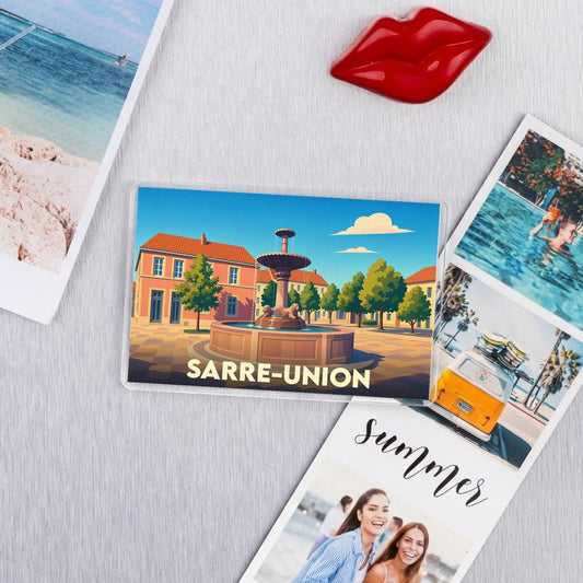 Magnet rectangulaire souvenir de la ville de Sarre-Union avec une illustration stylisée de sa fontaine et de ses façades colorées.