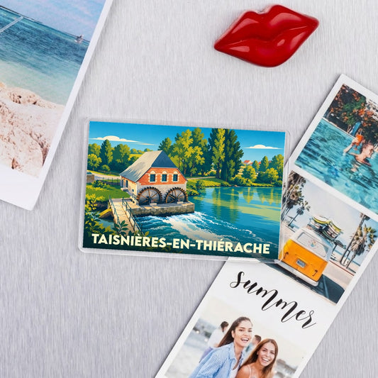 Magnet souvenir de la ville de Taisnières-en-Thiérache illustrant un moulin à eau au bord d'une rivière.