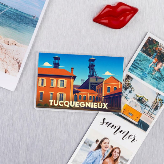 Magnet souvenir de la ville de Tucquegnieux avec une illustration stylisée d'anciens bâtiments miniers.