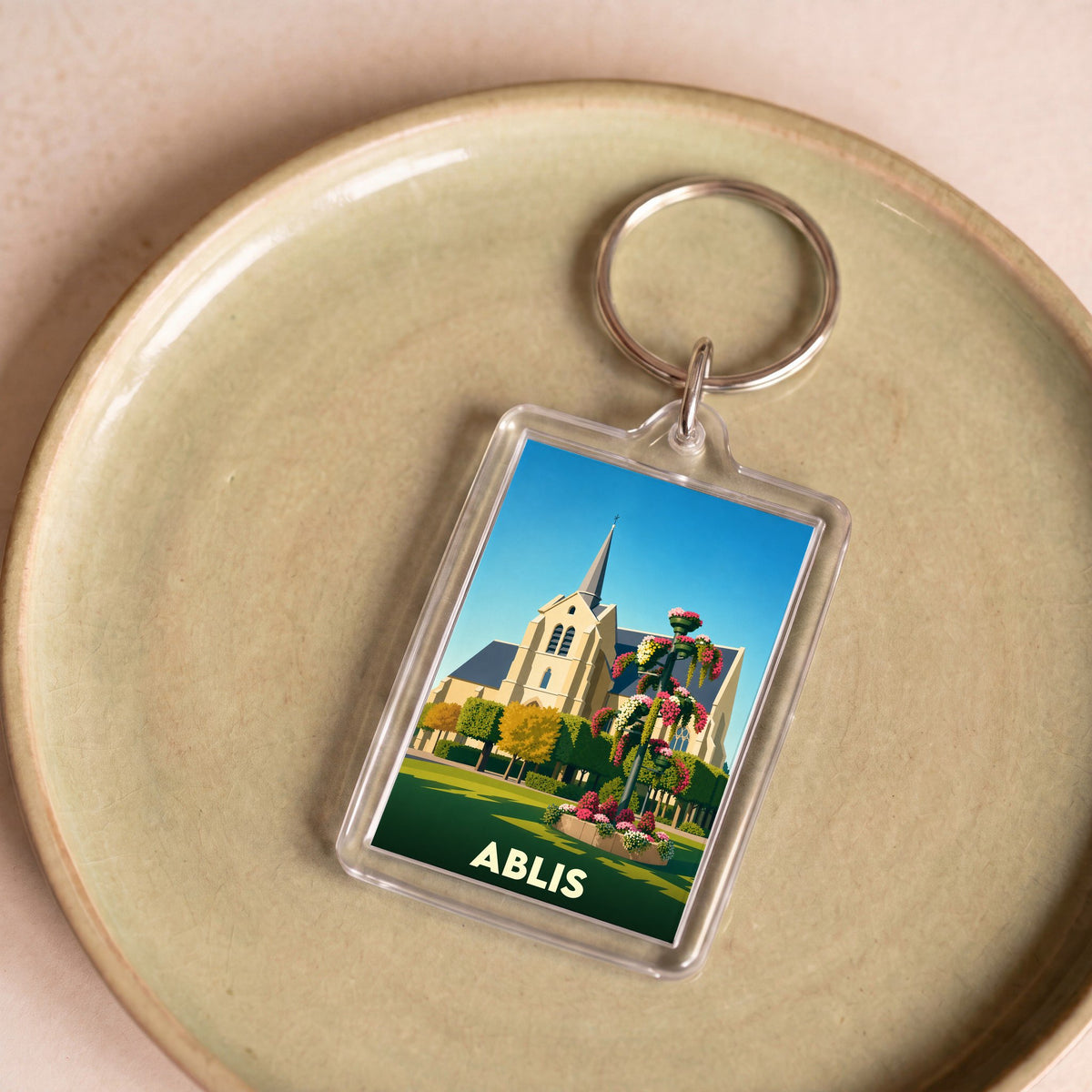 Porte-clés souvenir de la ville d'Ablis avec une illustration stylisée de son église et de jardins fleuris.