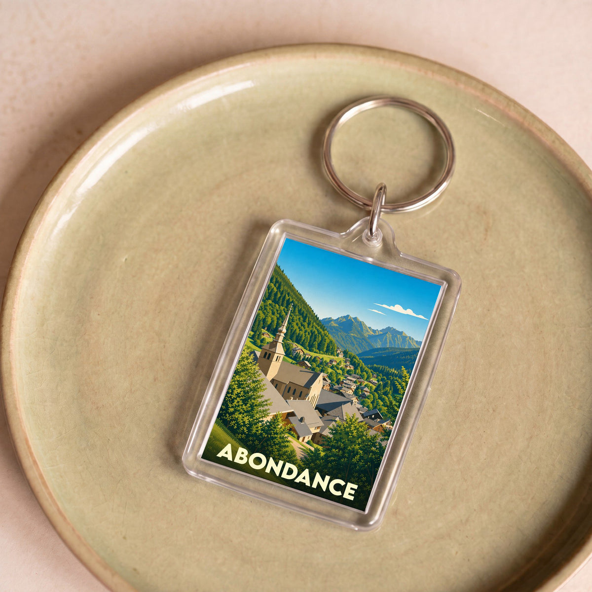 Porte-clés souvenir de la ville d'Abondance avec une illustration stylisée de son église et des montagnes environnantes.