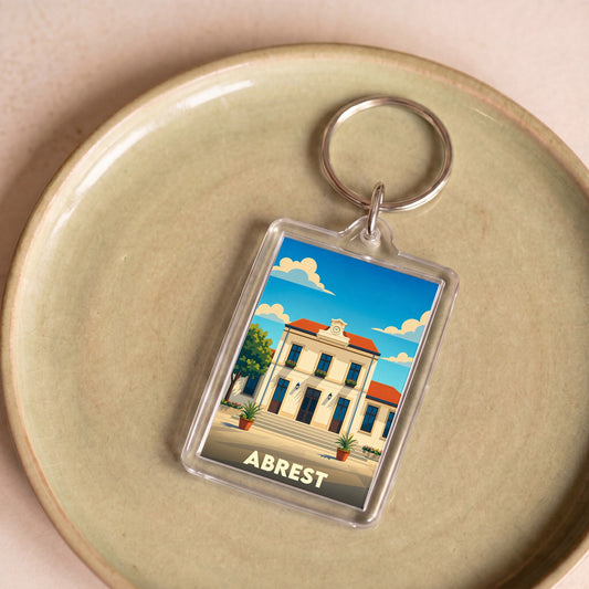 Porte-clés souvenir de la ville d'Abrest avec une illustration stylisée de sa mairie sous un ciel bleu.