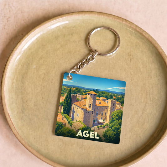 Porte-clés souvenir de la ville de Agel illustré d'un paysage de village médiéval stylisé.