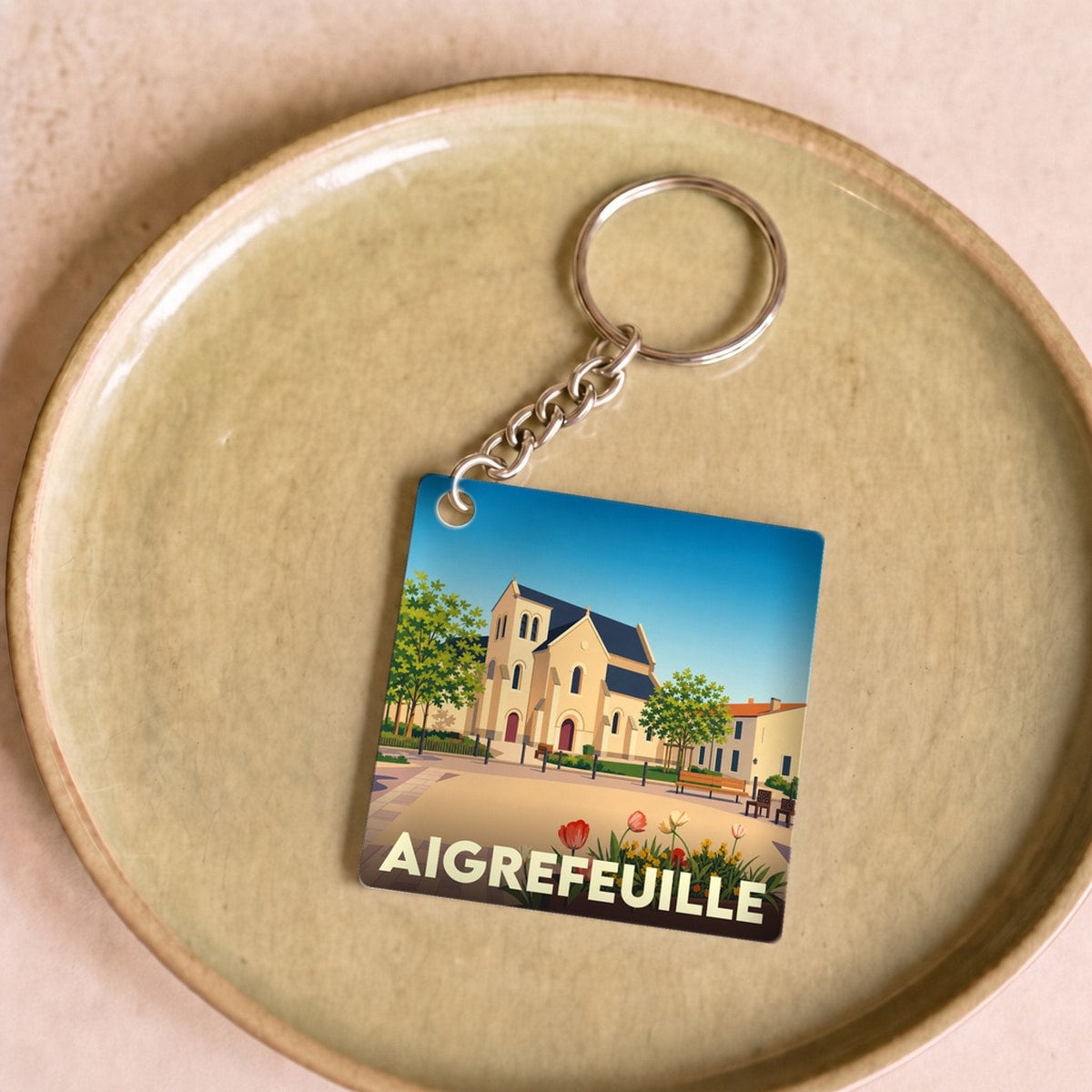 Porte-clés souvenir de la ville d'Aigrefeuille avec une illustration stylisée de son église.