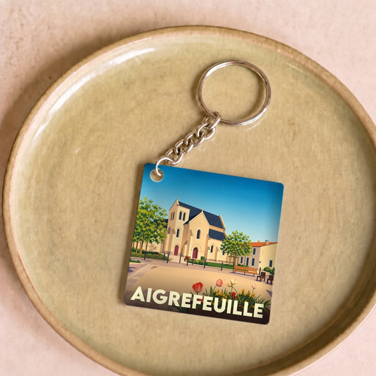 Porte-clés souvenir de la ville d'Aigrefeuille avec une illustration stylisée de son église.