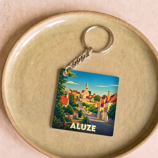 Porte-clés souvenir de la ville de Aluze avec une illustration stylisée d'un village ensoleillé.