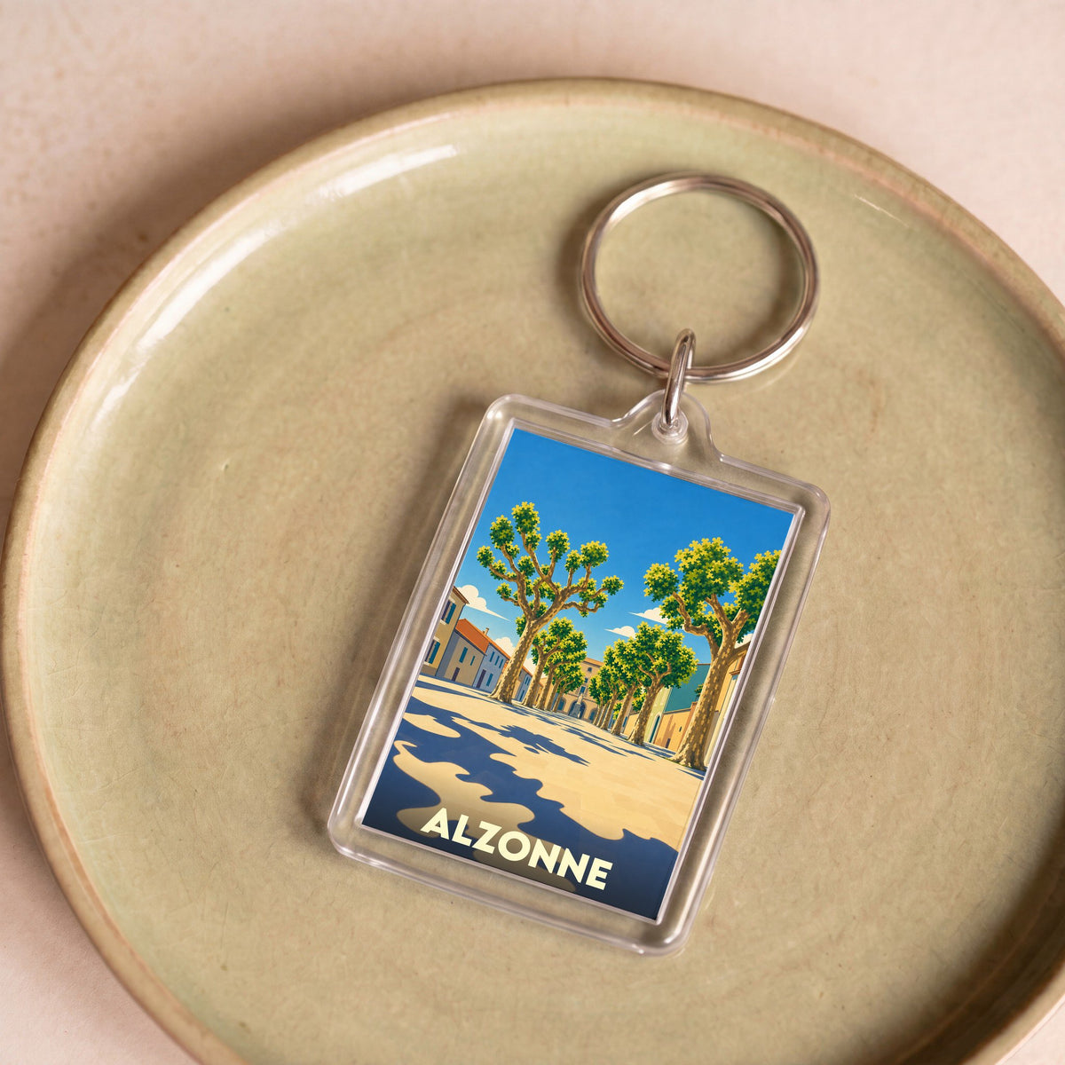 Porte-clés souvenir de la ville d'Alzonne avec une illustration stylisée d'une rue bordée de platanes.