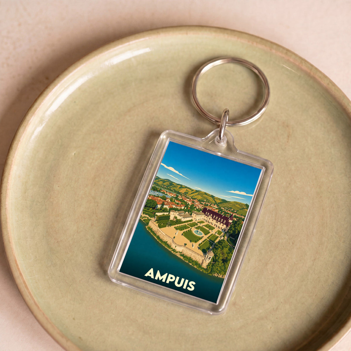 Porte-clés souvenir de la ville d'Ampuis avec une illustration stylisée de son château au bord de l'eau.