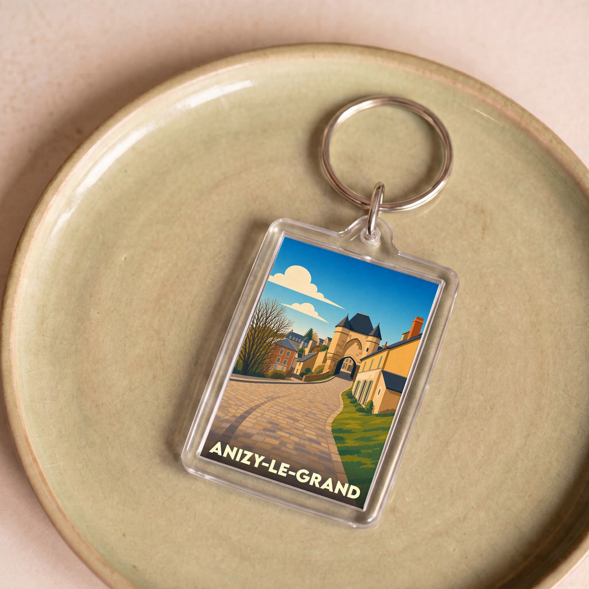 Porte-clés souvenir de la ville d'Anizy-le-Grand avec une illustration stylisée d'une rue pavée et de son architecture.