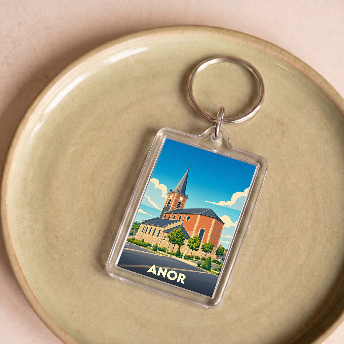 Porte-clés souvenir de la ville d'Anor avec une illustration stylisée de son église.