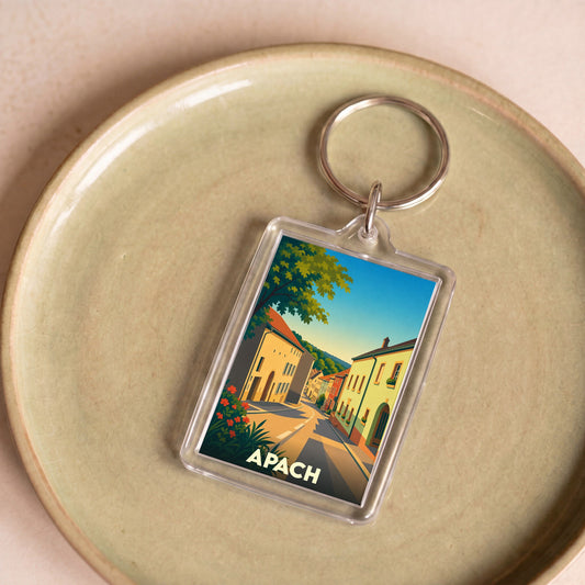 Porte-clés souvenir de la ville d'Apach avec une illustration colorée et stylisée de ses rues.