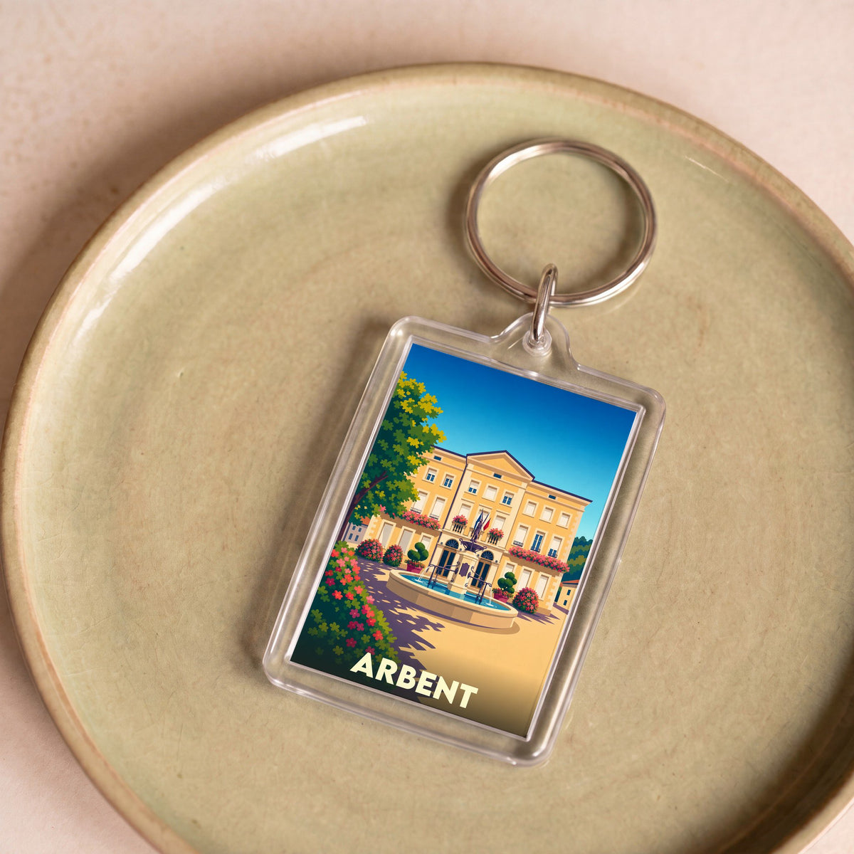 Porte-clés souvenir de la ville d'Arbent avec une illustration stylisée de sa mairie et d'une fontaine.