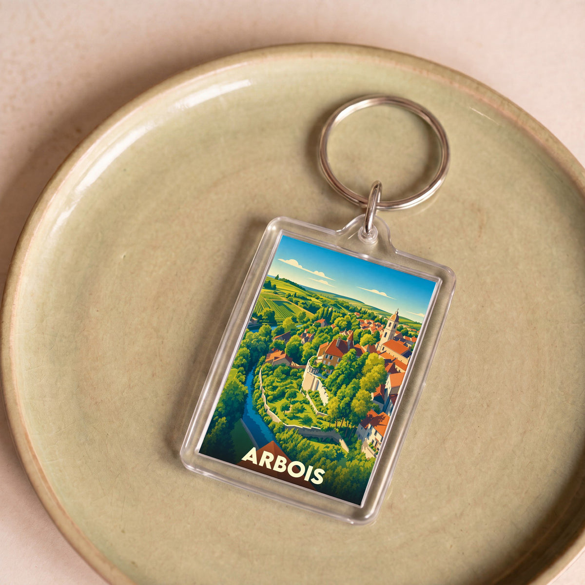 Porte-clés souvenir de la ville d'Arbois avec une illustration colorée de ses paysages et de son architecture.