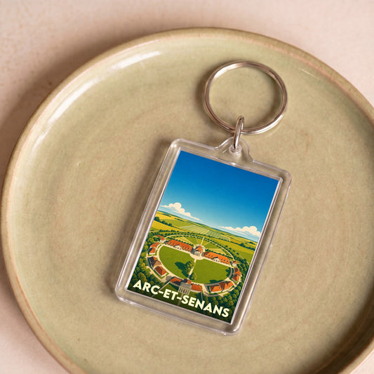 Porte-clés souvenir de la ville d’Arc-et-Senans illustré par une vue aérienne stylisée de la Saline royale.