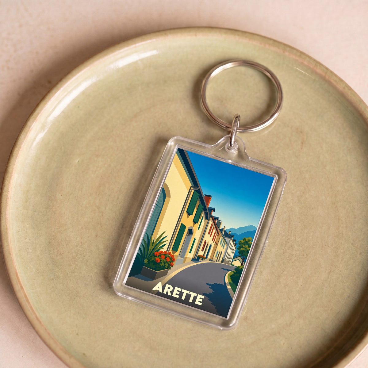 Porte-clés souvenir de la ville d'Arette avec une illustration stylisée d'une rue pittoresque.