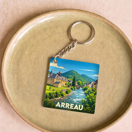 Porte-clés souvenir de la ville d'Arreau avec une illustration stylisée d'un paysage montagneux et d'une rivière.