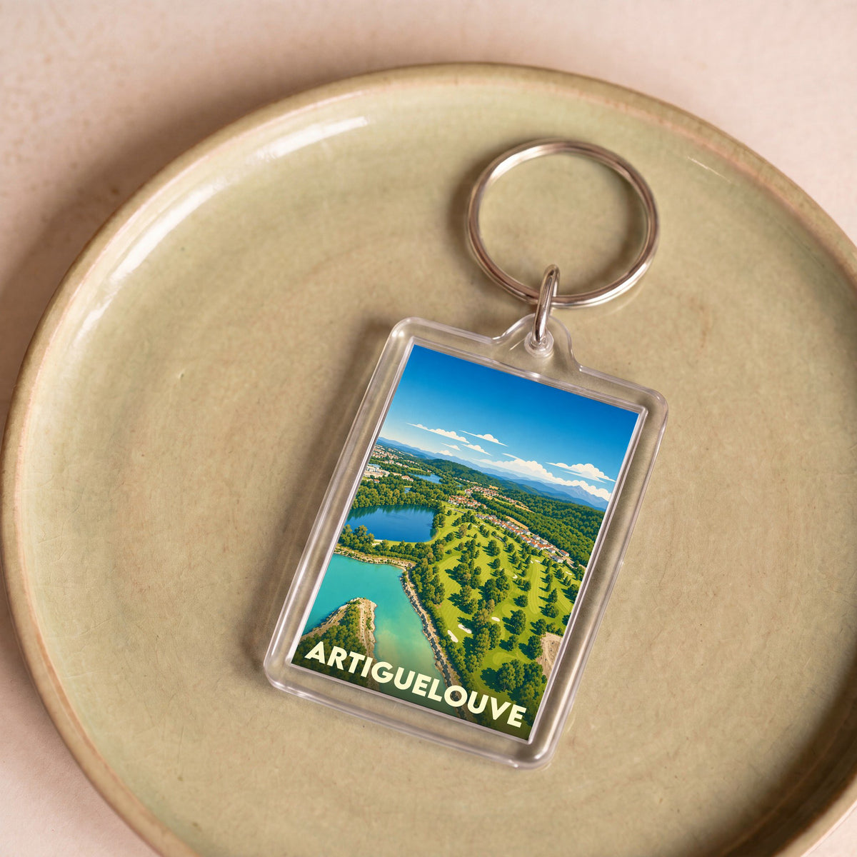 Porte-clés souvenir de la ville d'Artiguelouve avec une illustration stylisée de son paysage.