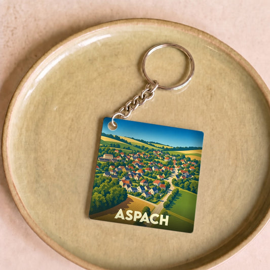 Porte-clés souvenir de la ville de Aspach avec une illustration stylisée d'un village entouré de champs.