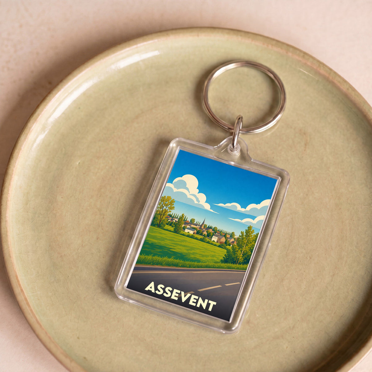 Porte-clés souvenir de la ville d'Assevent avec une illustration stylisée d'un paysage de campagne.