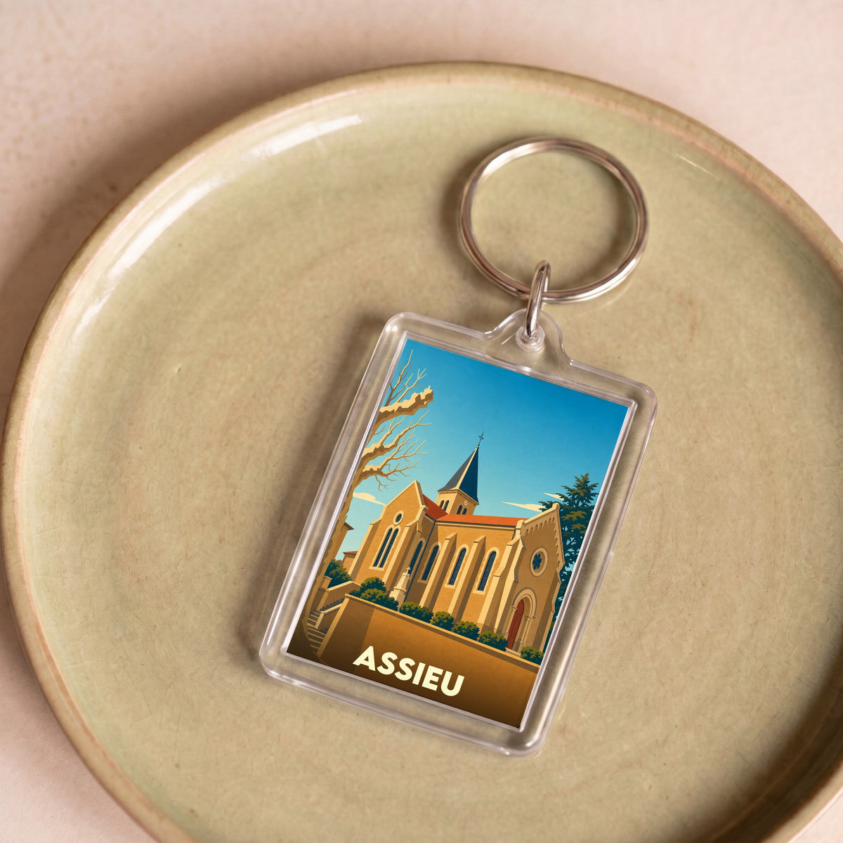 Porte-clés souvenir de la ville d'Assieu avec une illustration stylisée de son église.