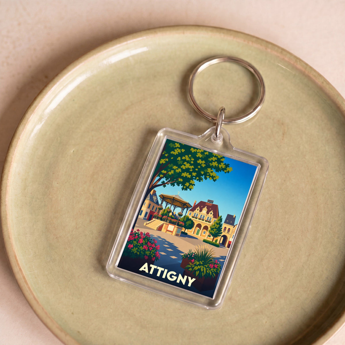Porte-clés souvenir de la ville d'Attigny avec une illustration stylisée de sa place centrale.