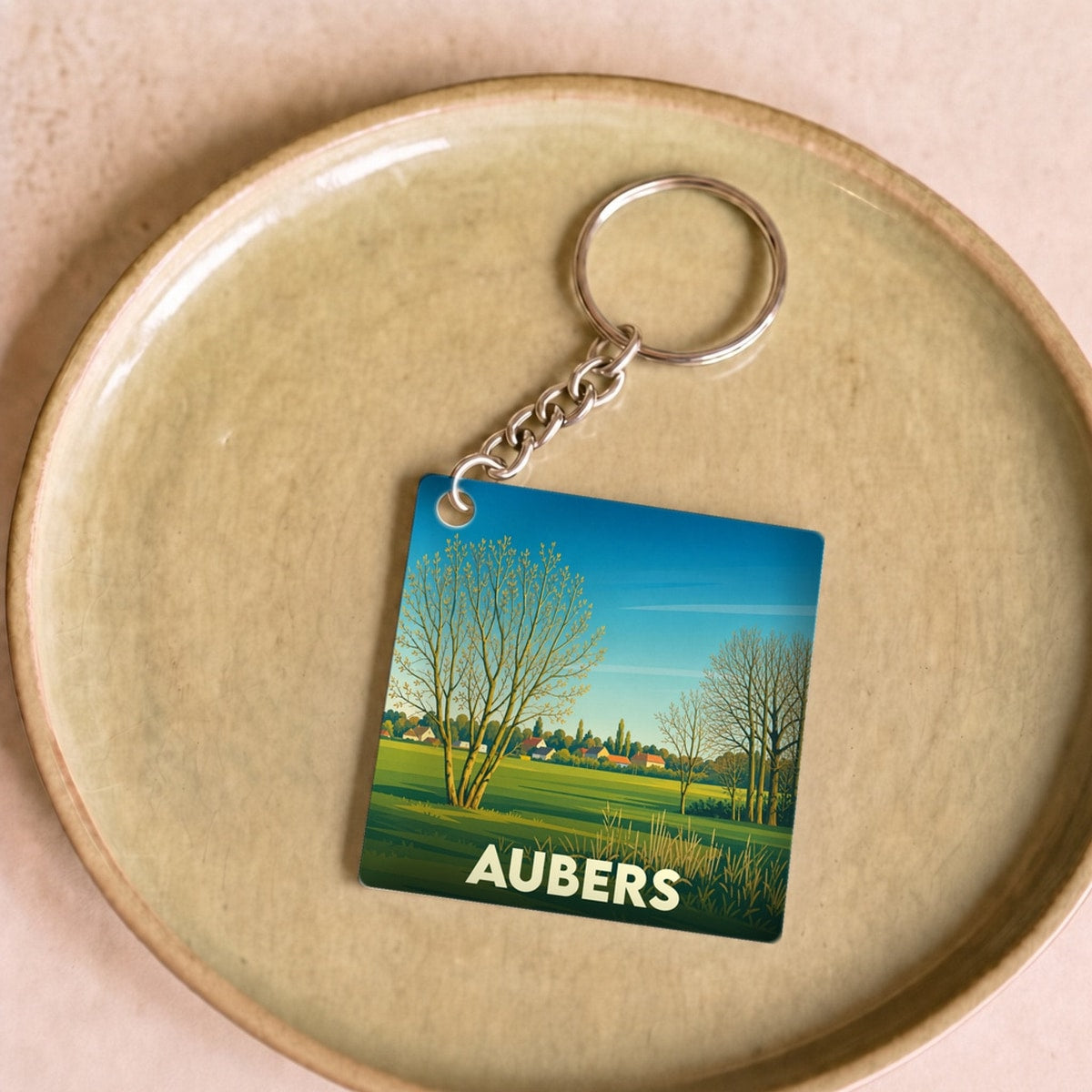 Porte-clés souvenir de la ville d'Aubers avec une illustration de paysage champêtre stylisé.