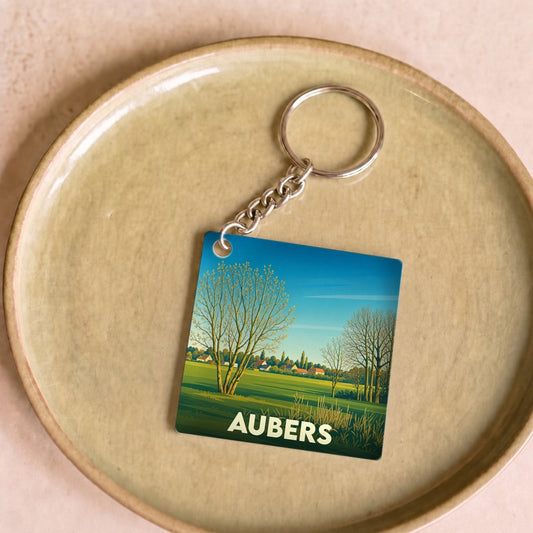 Porte-clés souvenir de la ville d'Aubers avec une illustration de paysage champêtre stylisé.