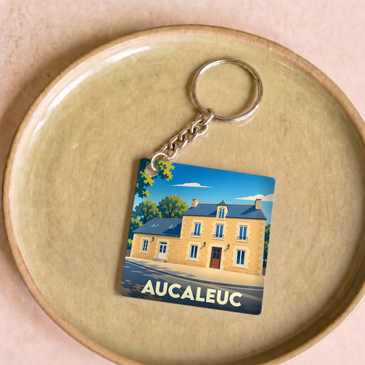 Porte-clés souvenir de la ville d'Aucaleuc avec une illustration stylisée d'une maison traditionnelle.