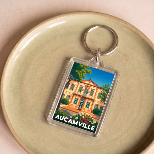 Porte-clés souvenir de la ville de Aucamville avec une illustration colorée et stylisée de sa mairie.
