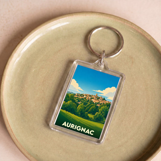 Porte-clés souvenir de la ville d'Aurignac avec une illustration stylisée de son paysage vallonné.