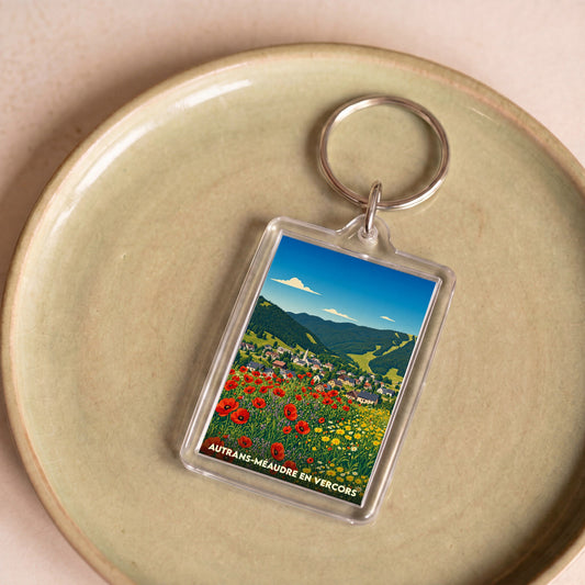 Porte-clés souvenir de la ville d'Autrans-Méaudre en Vercors avec une illustration stylisée d'un paysage de montagne fleuri.