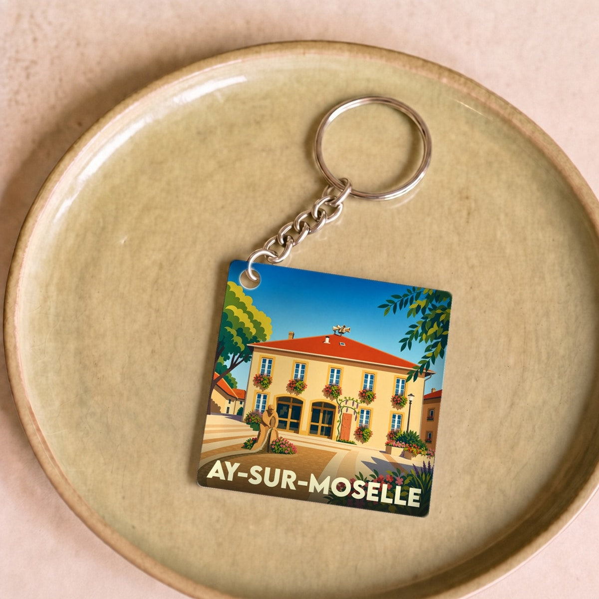 Porte-clés souvenir de la ville d'Ay-sur-Moselle avec une illustration stylisée.