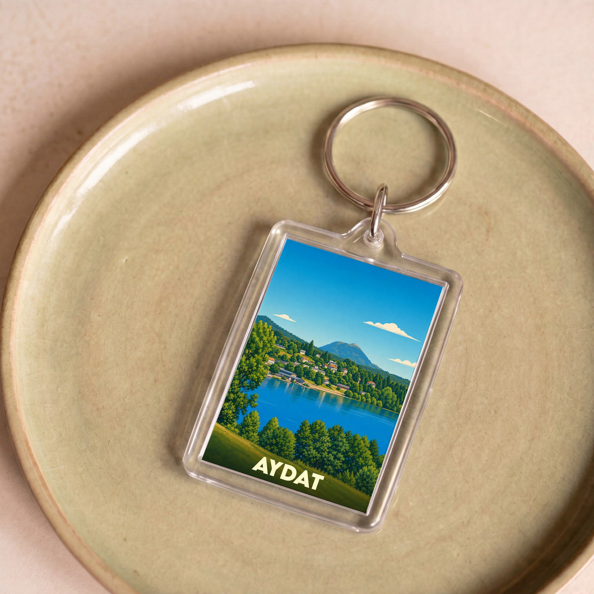 Porte-clés souvenir de la ville d'Aydat avec une illustration stylisée de son lac et des montagnes.